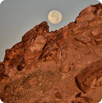 Photograph of the moon rising above a desert landscape.